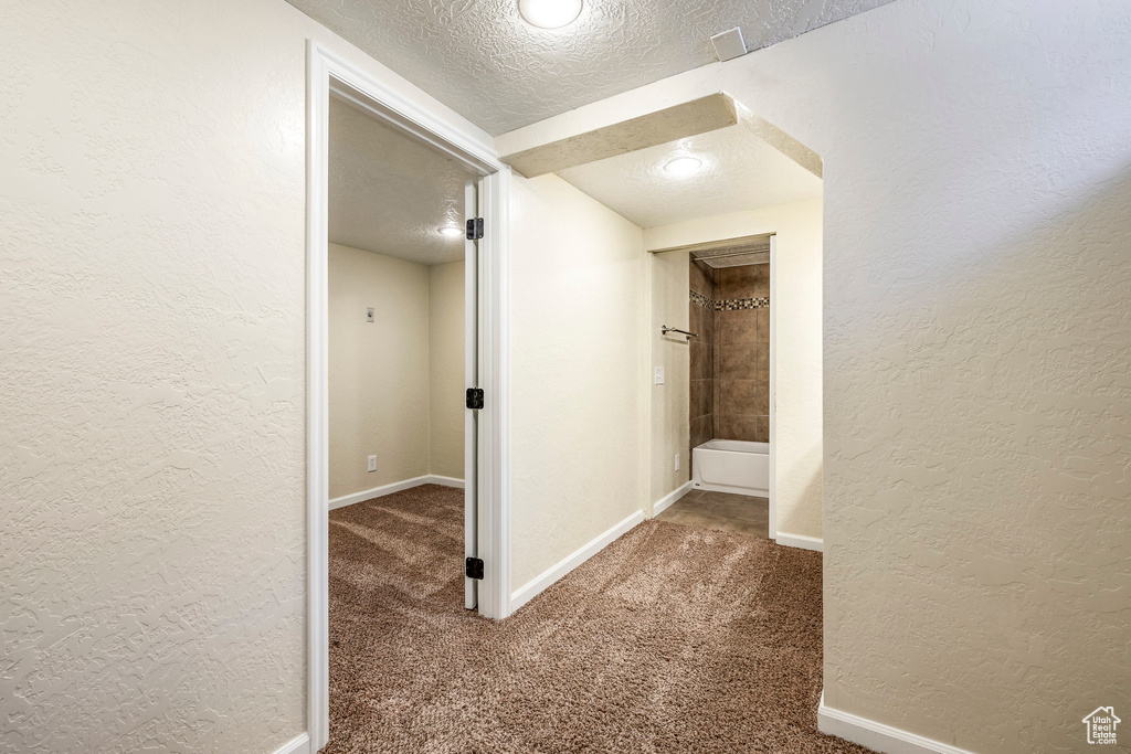 Corridor with a textured ceiling, a textured wall, and carpet floors