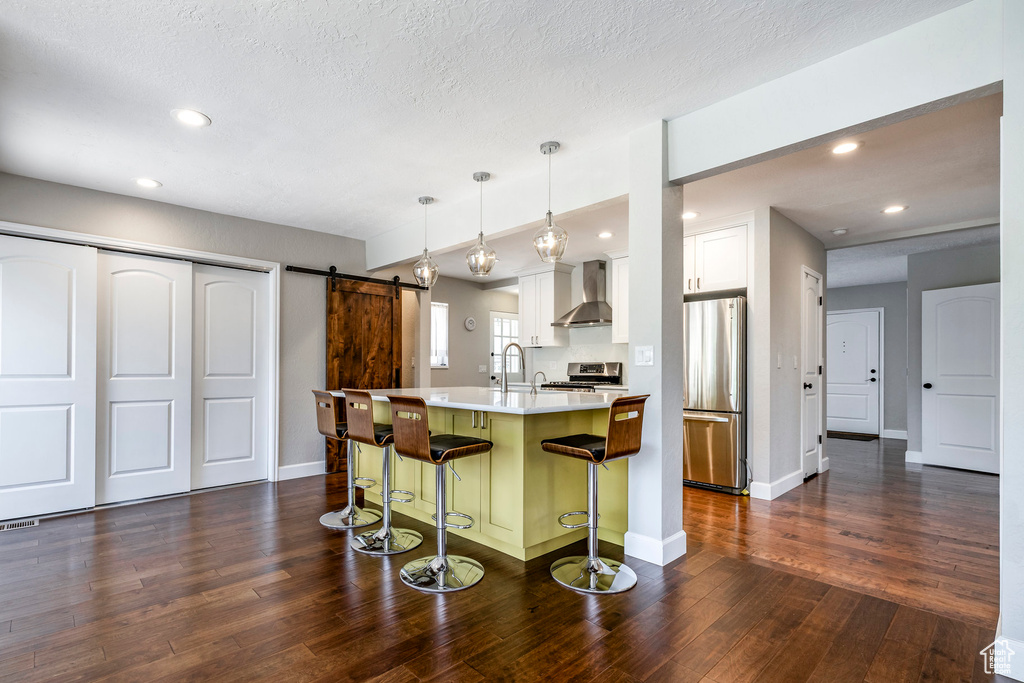 Kitchen featuring wall chimney exhaust hood, stainless steel appliances, a barn door, a breakfast bar area, and dark wood finished floors