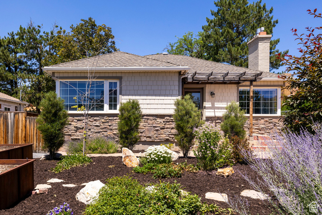 View of front facade with stone siding, a chimney, a pergola, and roof with shingles
