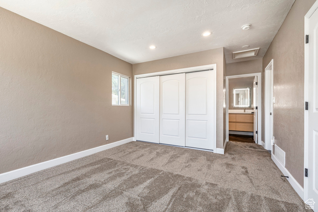 Unfurnished bedroom with attic access, carpet flooring, a closet, and a textured wall