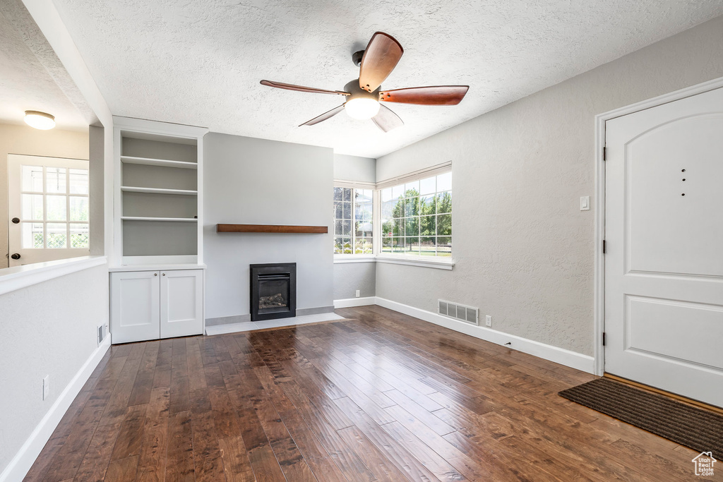 Unfurnished living room with a textured ceiling, a glass covered fireplace, wood-type flooring, ceiling fan, and built in features