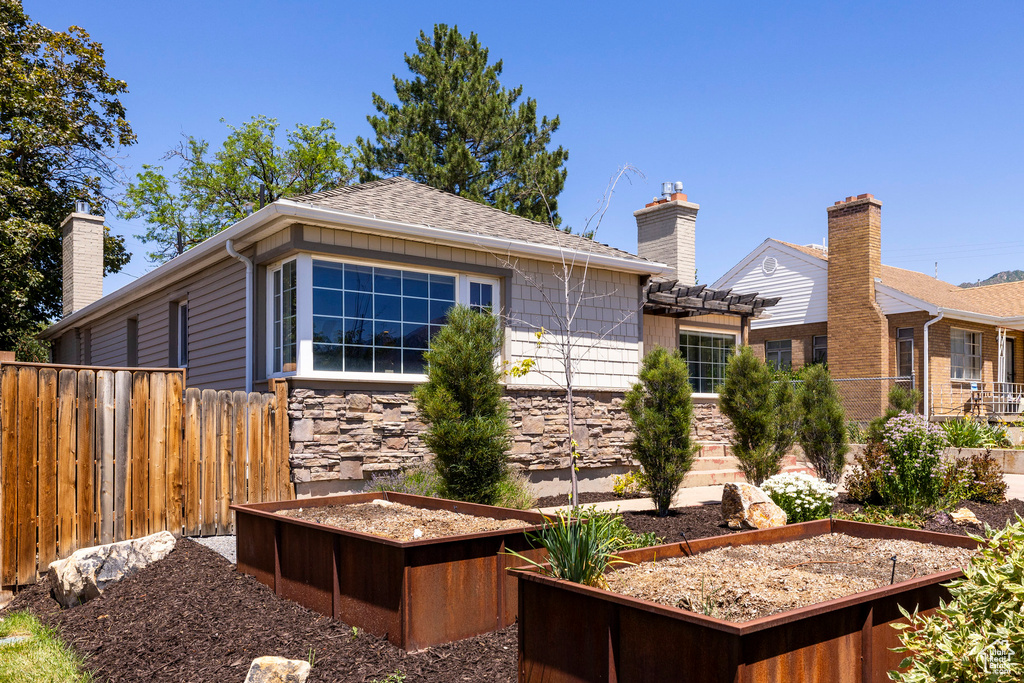 Rear view of house featuring a vegetable garden, a chimney, stone siding, and roof with shingles