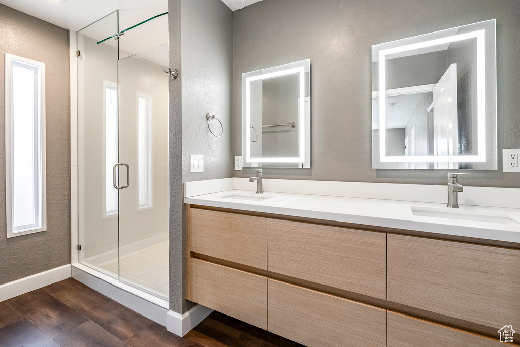 Full bath with a textured wall, a shower stall, wood finished floors, and double vanity