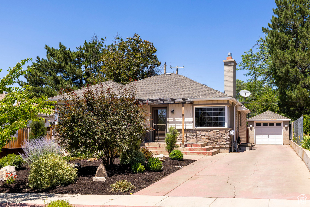 Bungalow-style home featuring an outdoor structure, driveway, a garage, a chimney, and roof with shingles