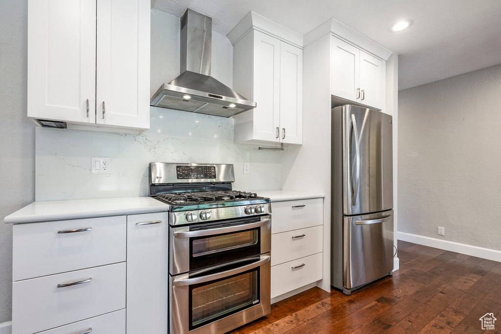 Kitchen featuring wall chimney range hood, stainless steel appliances, dark wood finished floors, light countertops, and white cabinetry