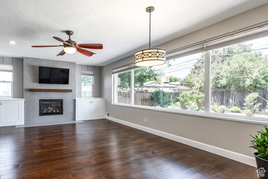 Unfurnished living room featuring wood finished floors, a glass covered fireplace, and a ceiling fan