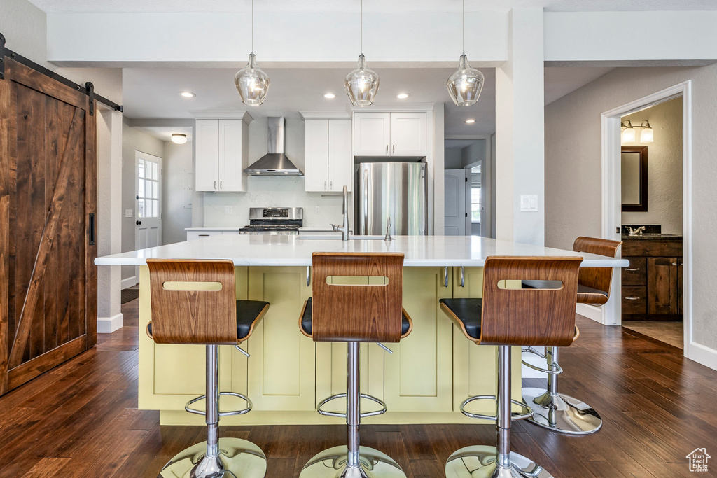 Kitchen with wall chimney exhaust hood, stainless steel appliances, dark wood-style floors, a center island with sink, and recessed lighting