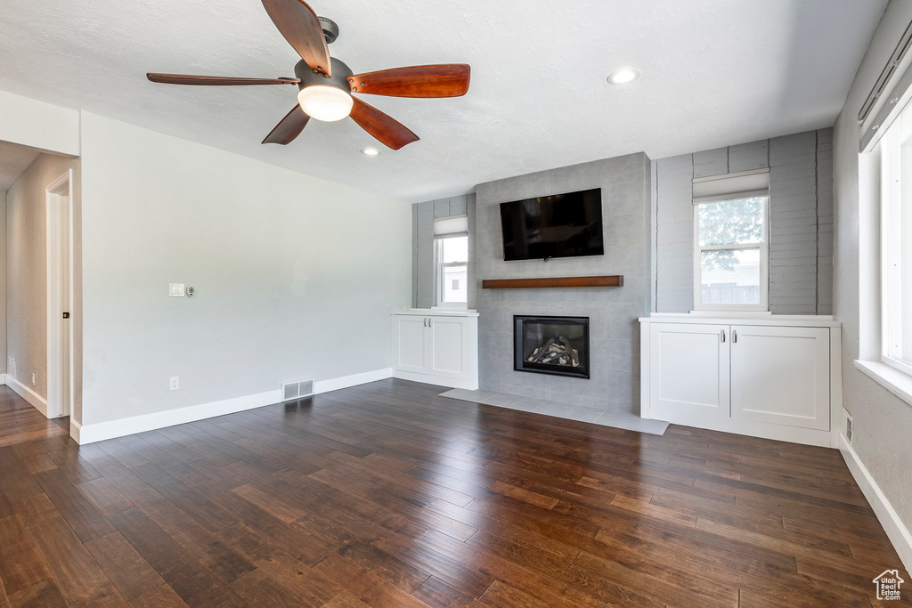 Unfurnished living room with plenty of natural light, a large fireplace, ceiling fan, dark wood-style flooring, and recessed lighting