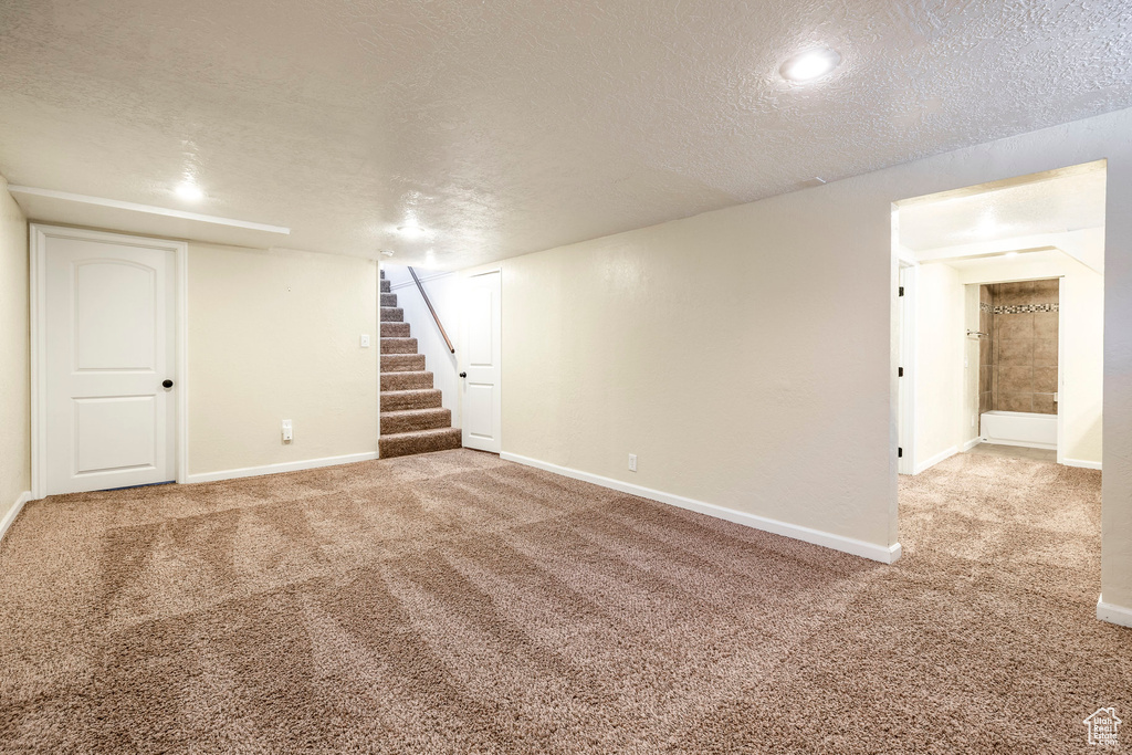 Finished below grade area featuring a textured ceiling, carpet, and stairs
