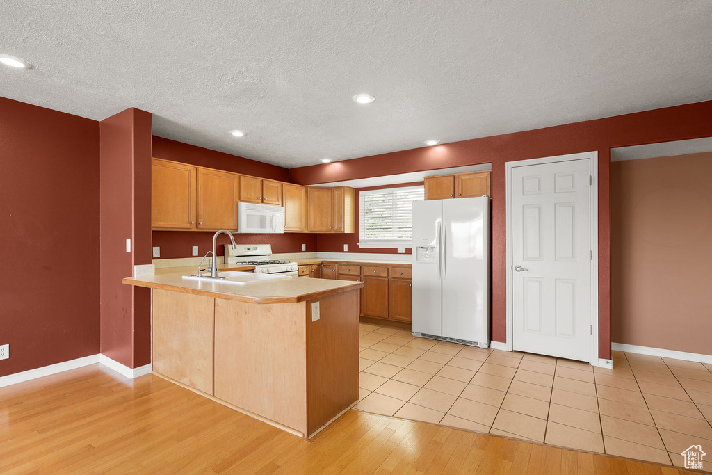 Kitchen featuring white appliances, a peninsula, light countertops, a textured ceiling, and light wood-style flooring
