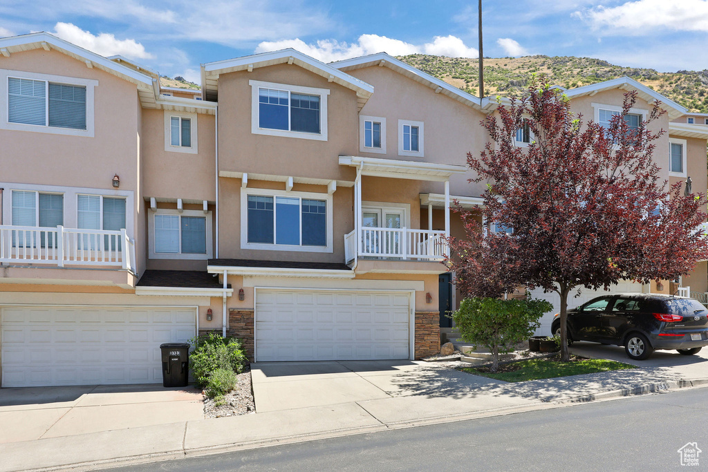 Multi unit property with stucco siding, an attached garage, concrete driveway, stone siding, and a mountain view