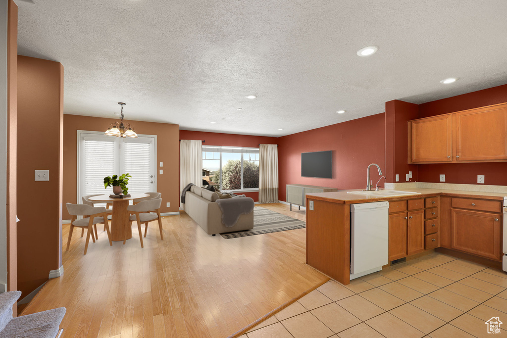 Kitchen with white dishwasher, a chandelier, open floor plan, light countertops, and a peninsula