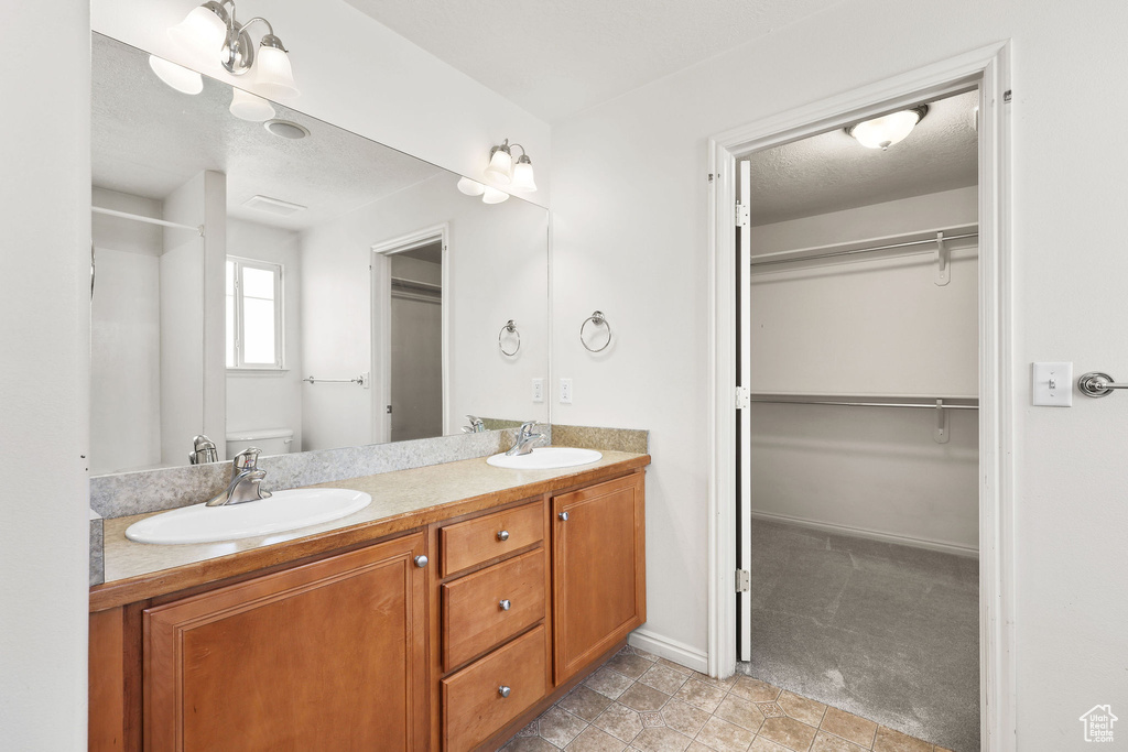 Bathroom featuring double vanity, a walk in closet, and a textured ceiling