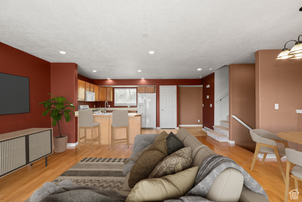 Living room featuring light wood finished floors, stairs, a textured ceiling, and recessed lighting
