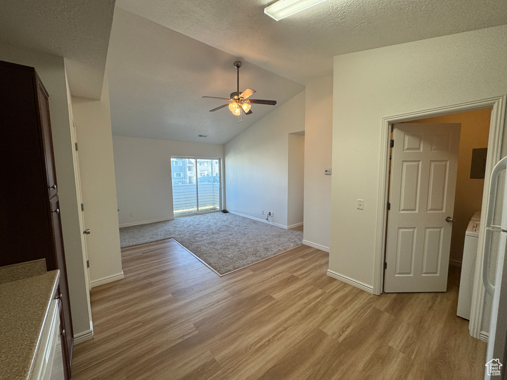 Unfurnished room with light wood-style floors, vaulted ceiling, a ceiling fan, and a textured ceiling