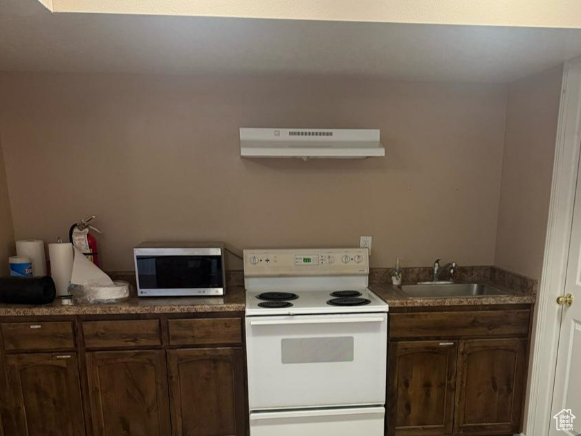 Kitchen with white electric range oven, stainless steel microwave, under cabinet range hood, light tile patterned floors, and dark brown cabinetry