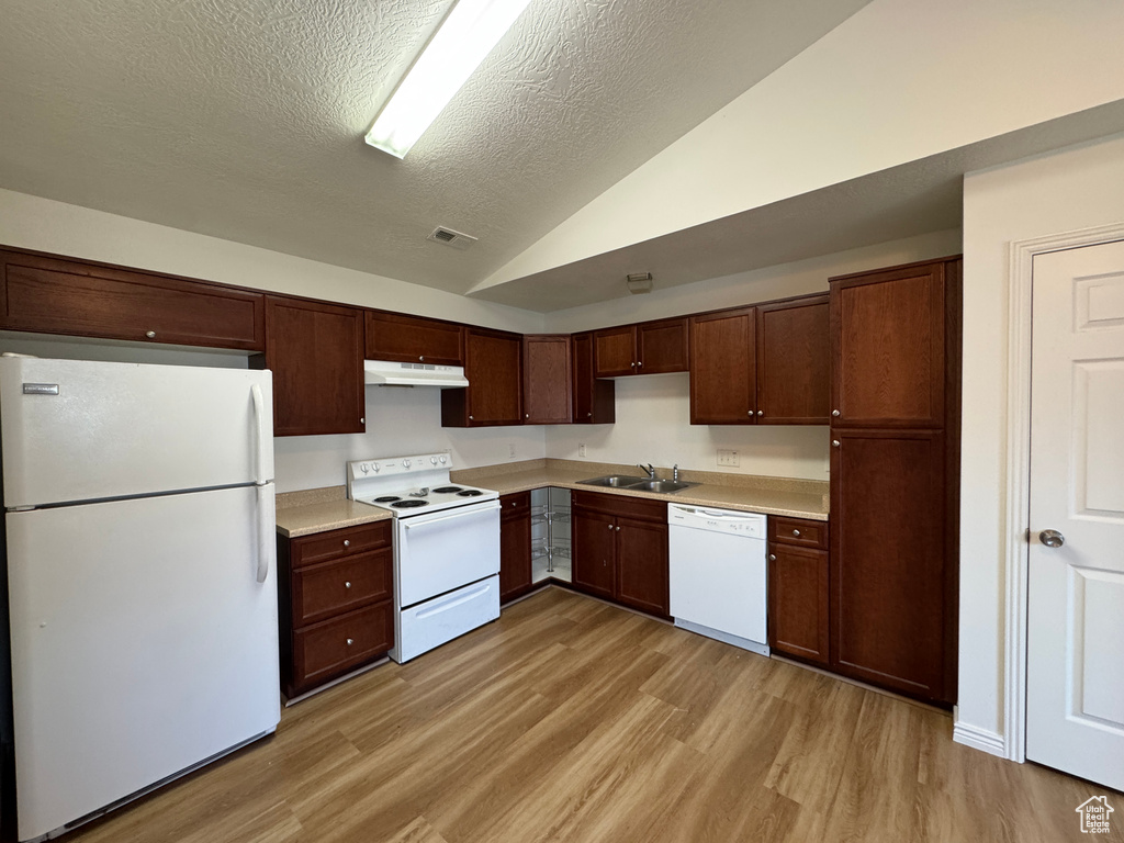 Kitchen with white appliances, under cabinet range hood, vaulted ceiling, light wood-style floors, and light countertops