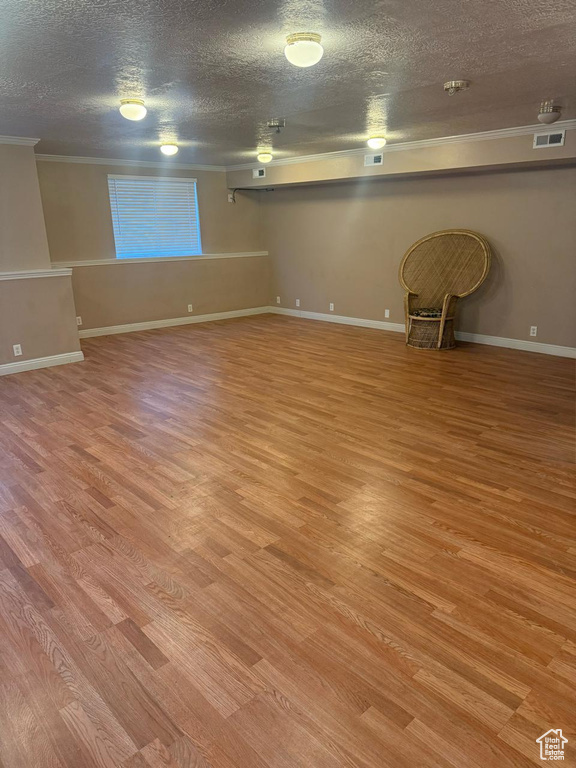 Finished below grade area with crown molding, a textured ceiling, and light wood-style flooring