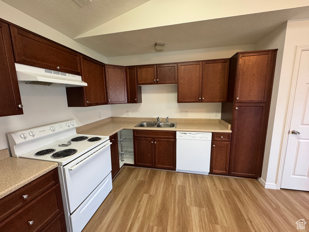 Kitchen with white appliances, under cabinet range hood, light wood finished floors, light countertops, and lofted ceiling