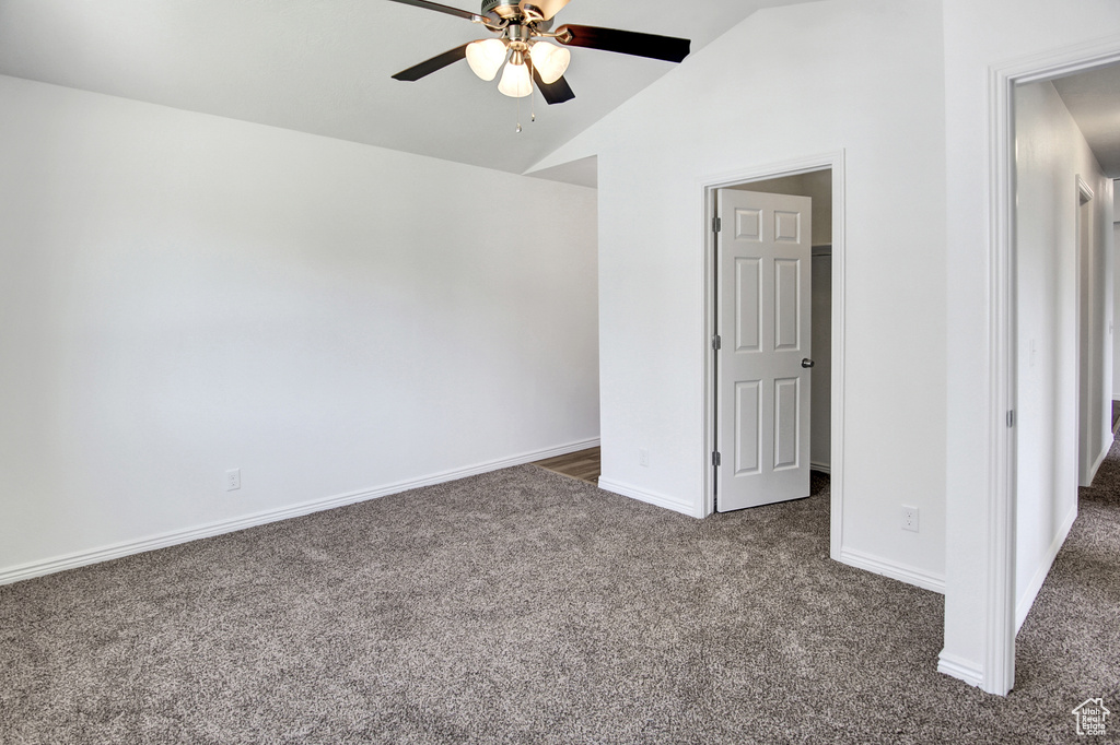Spare room featuring dark colored carpet, ceiling fan, and vaulted ceiling