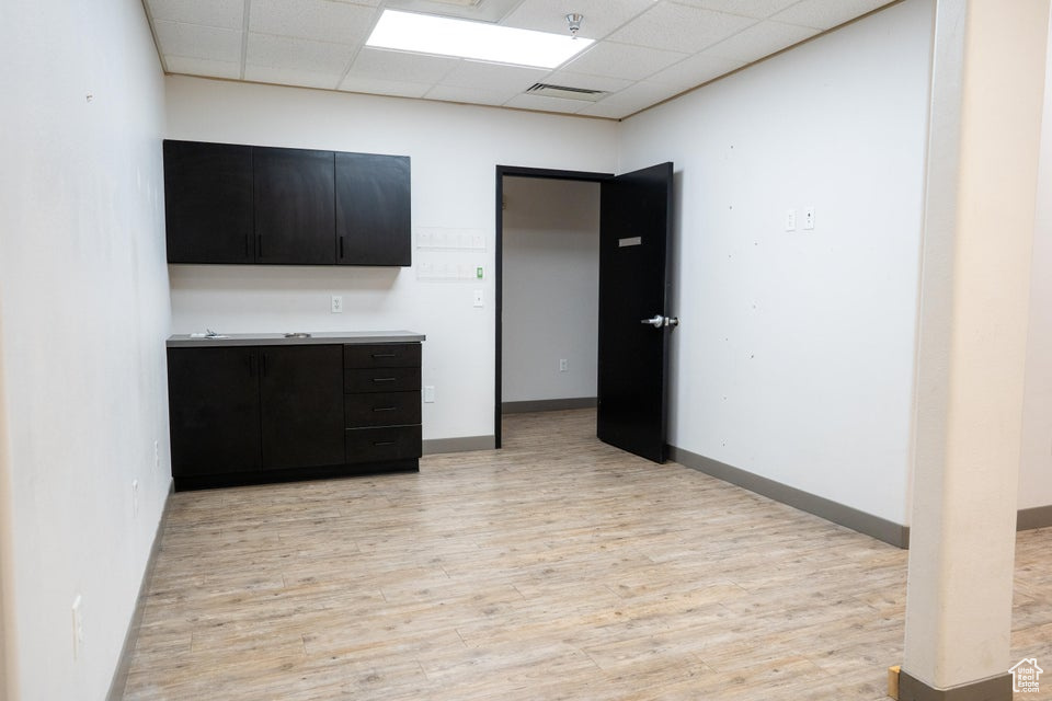 Kitchen with dark cabinets, light wood-type flooring, a paneled ceiling, and light countertops