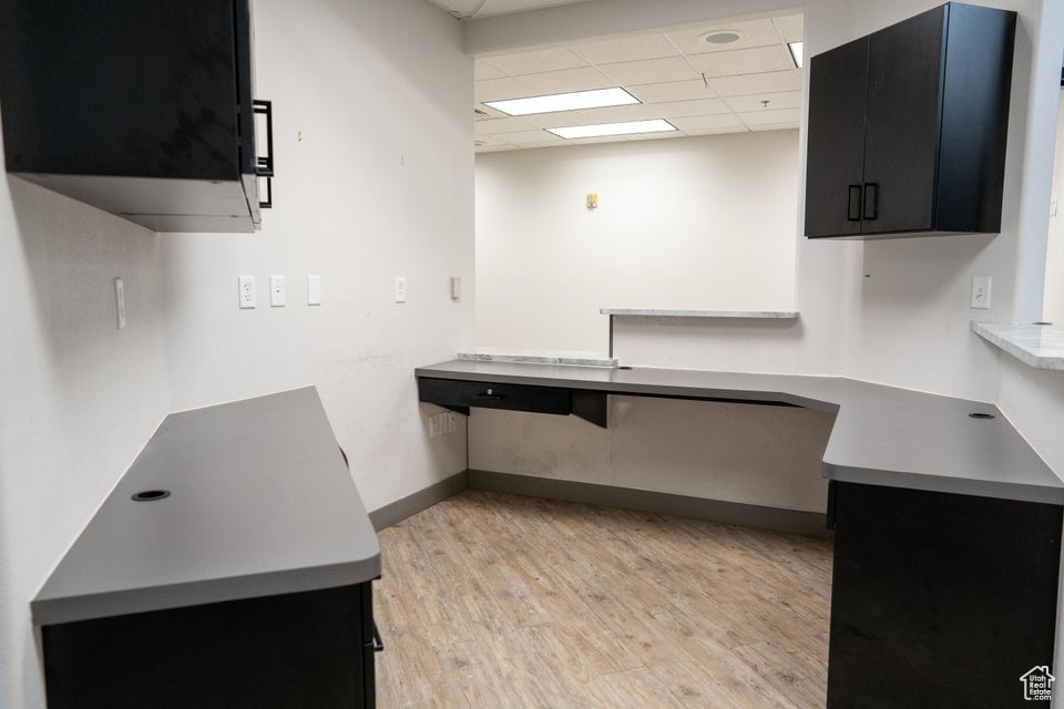 Kitchen with dark cabinets, a drop ceiling, light wood-style floors, and light countertops