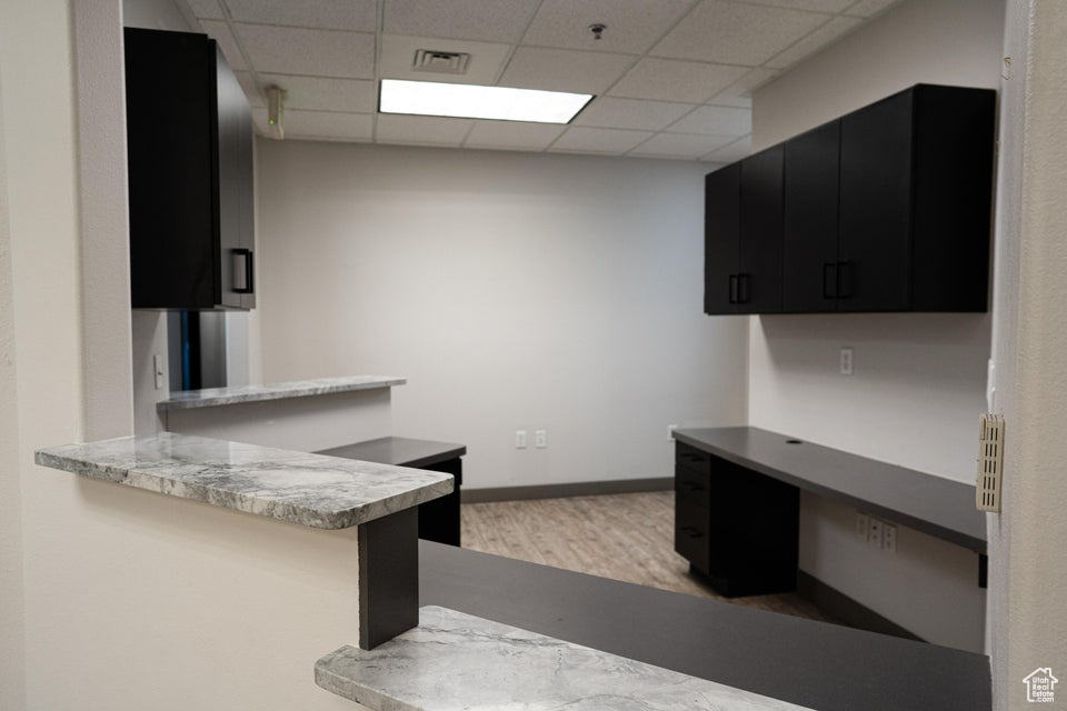 Kitchen with dark cabinetry, a drop ceiling, wood finished floors, a peninsula, and light countertops