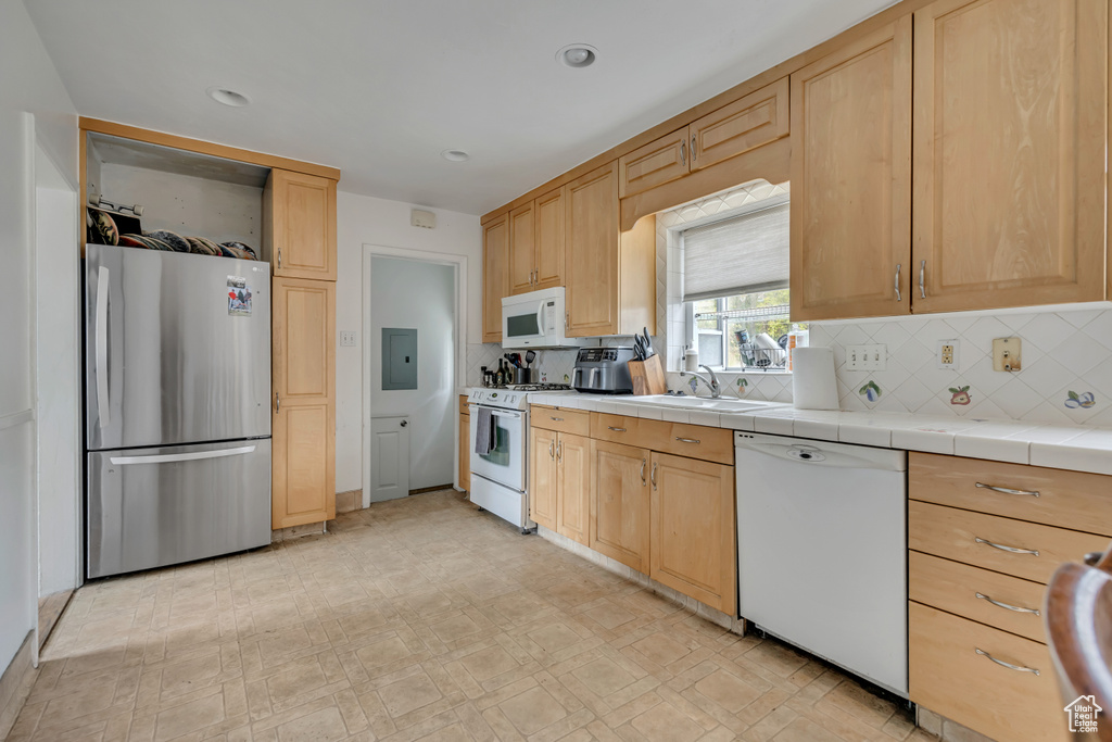Kitchen featuring white appliances, light brown cabinets, electric panel, decorative backsplash, and light flooring