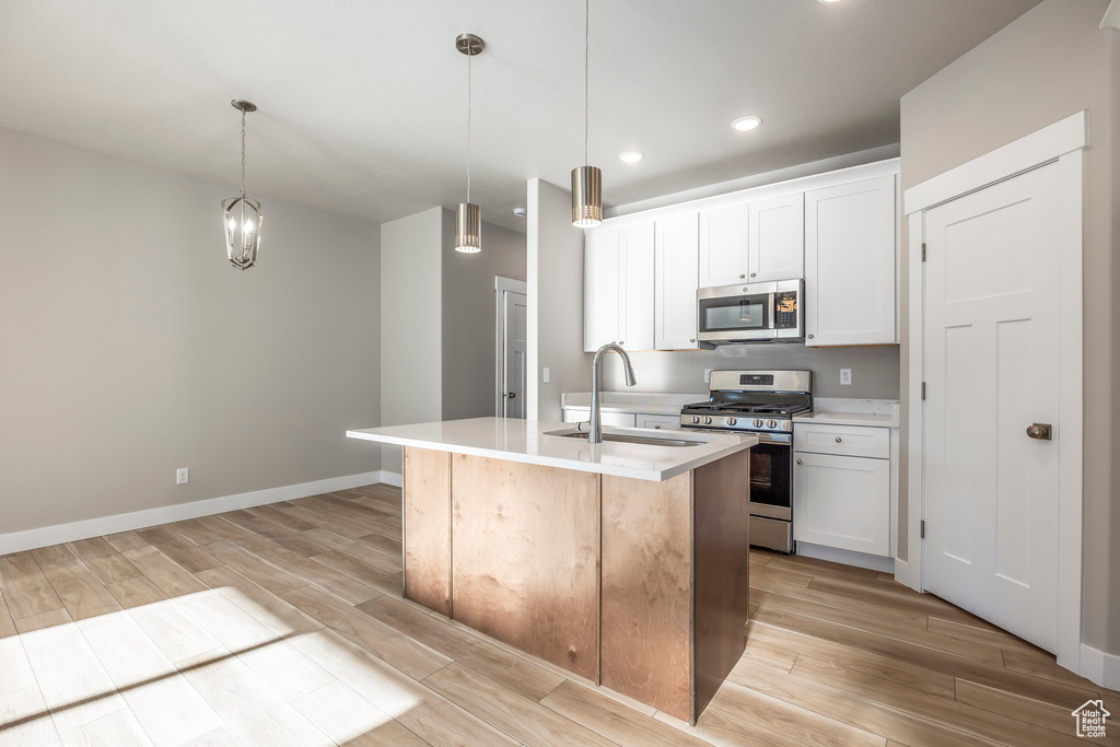 Kitchen featuring appliances with stainless steel finishes, light wood-type flooring, light countertops, a center island with sink, and recessed lighting