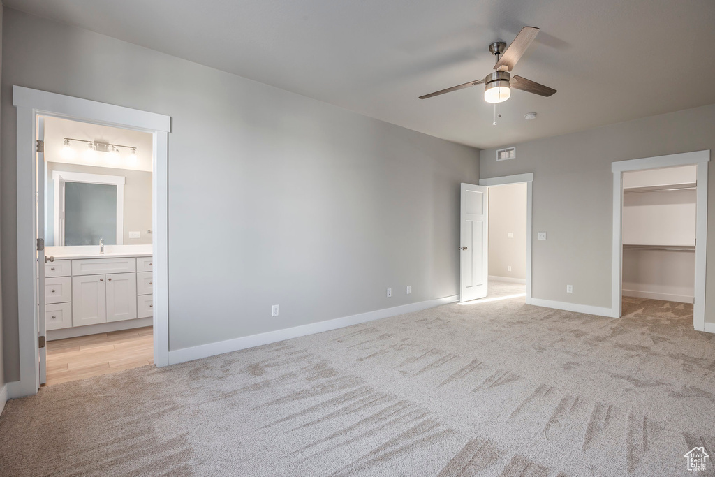 Unfurnished bedroom featuring light colored carpet, a spacious closet, ensuite bathroom, and ceiling fan