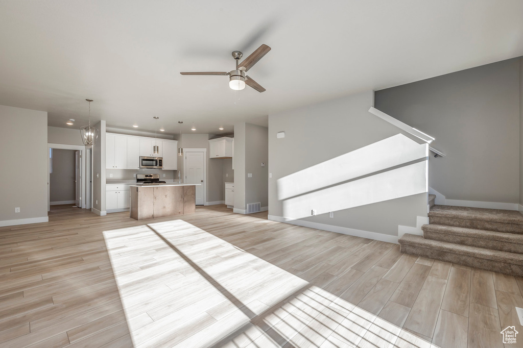 Unfurnished living room featuring ceiling fan, light wood-type flooring, stairs, recessed lighting, and a chandelier