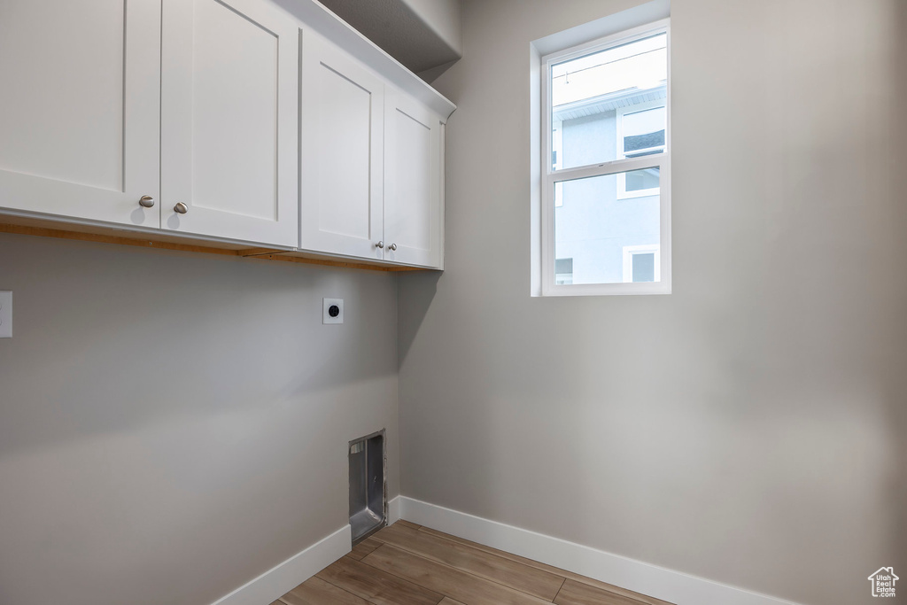 Laundry area with electric dryer hookup, cabinet space, and light wood finished floors