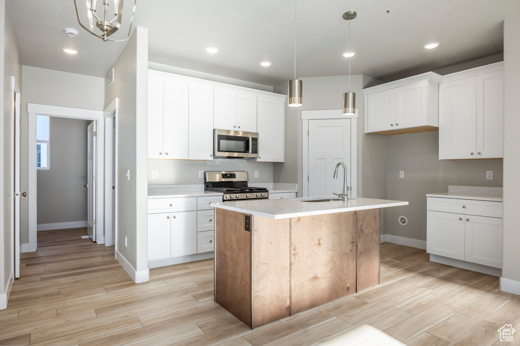Kitchen featuring stainless steel appliances, an island with sink, light countertops, white cabinets, and light wood-style floors