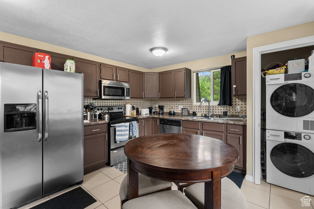 Kitchen featuring stainless steel appliances, stacked washer and clothes dryer, light tile patterned floors, backsplash, and dark brown cabinetry