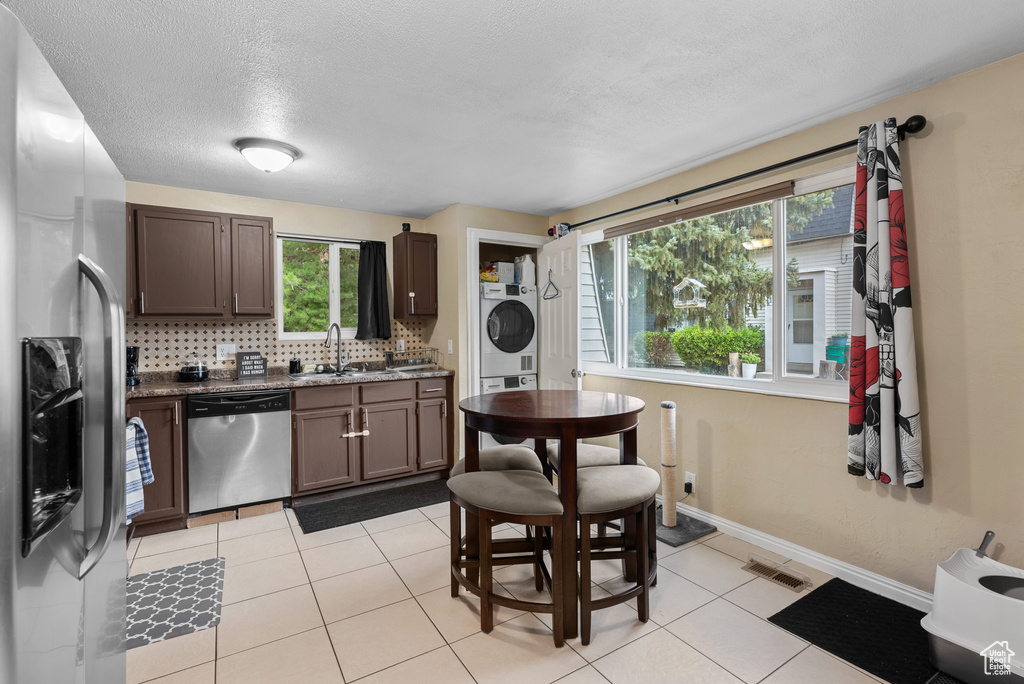 Kitchen featuring appliances with stainless steel finishes, stacked washer / dryer, decorative backsplash, light tile patterned floors, and dark stone counters