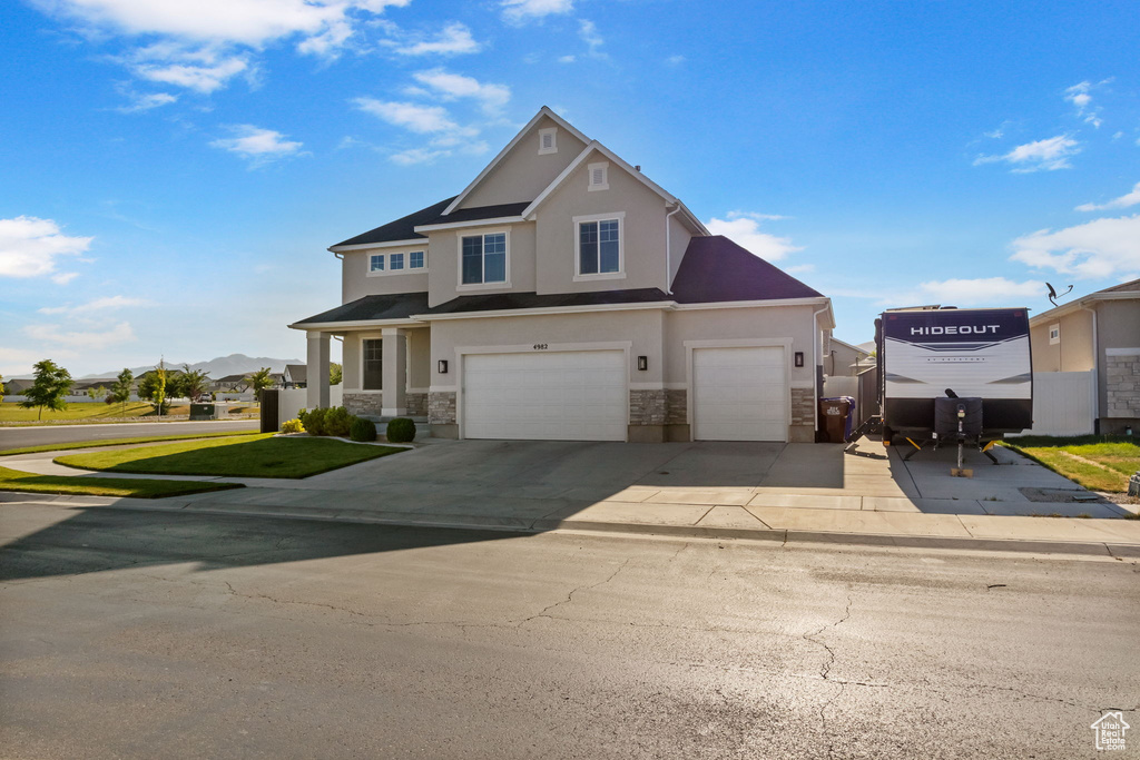 View of front of property featuring stone siding, stucco siding, driveway, and an attached garage