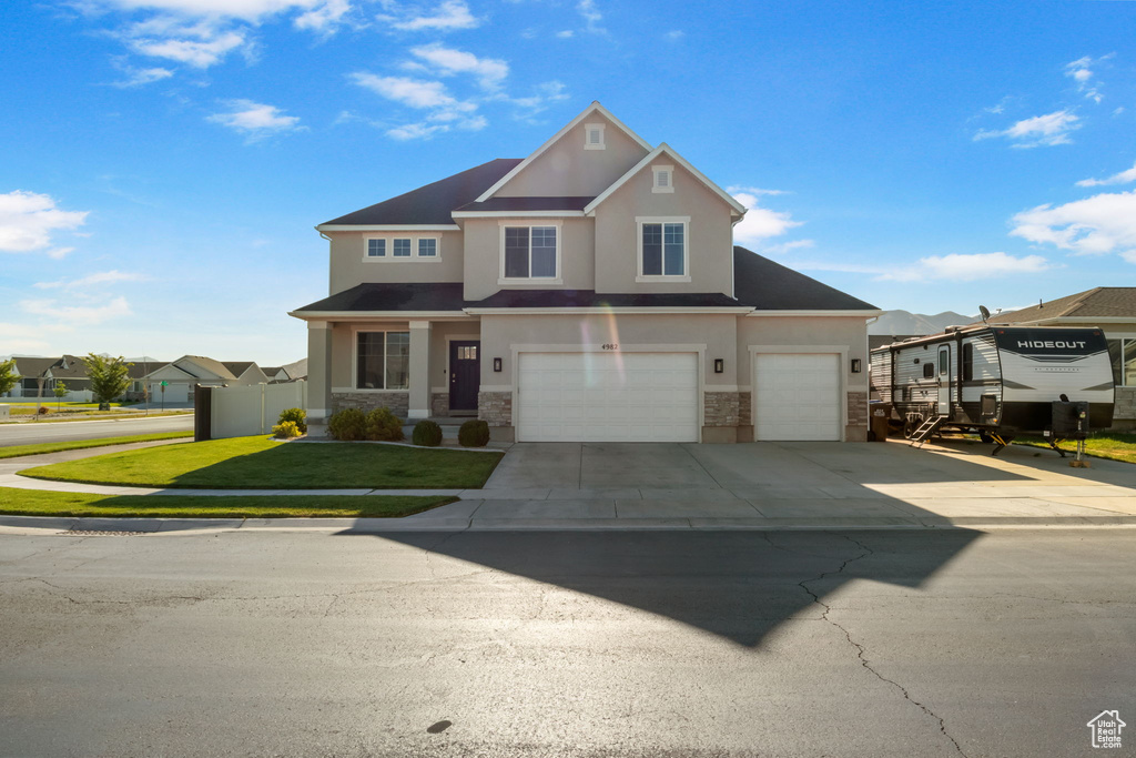 View of front facade with stone siding, stucco siding, driveway, a garage, and a residential view