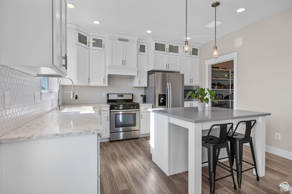 Kitchen featuring appliances with stainless steel finishes, decorative backsplash, white cabinetry, a kitchen breakfast bar, and recessed lighting