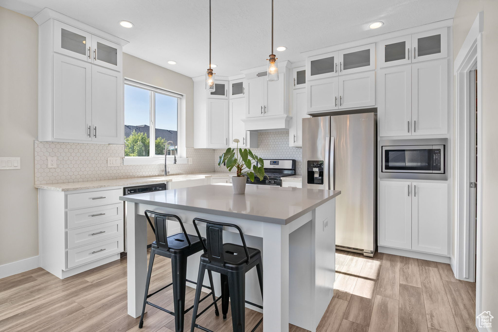 Kitchen featuring appliances with stainless steel finishes, light wood finished floors, white cabinetry, light countertops, and decorative backsplash