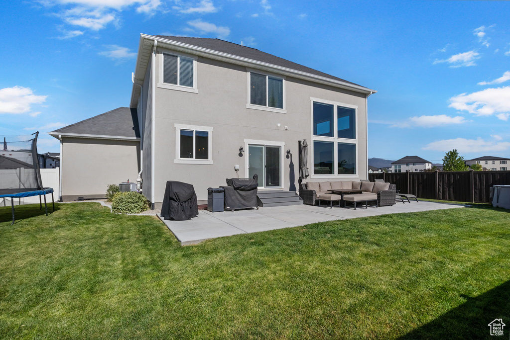 Back of property featuring a trampoline, outdoor lounge area, a patio, a fenced backyard, and stucco siding