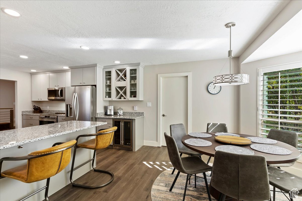 Dining space featuring beverage cooler, bar area, dark wood finished floors, recessed lighting, and a textured ceiling