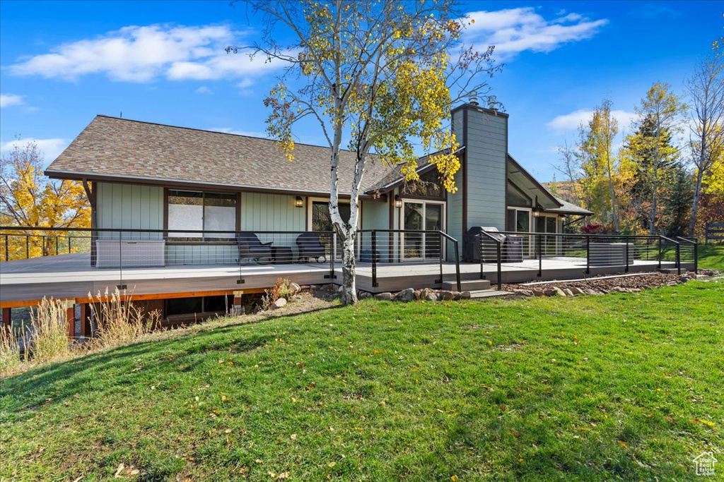 Back of house with a lawn, a chimney, a deck, and roof with shingles