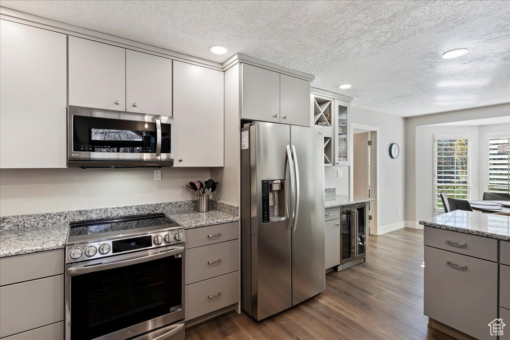 Kitchen with stainless steel appliances, gray cabinetry, wine cooler, dark wood finished floors, and a textured ceiling