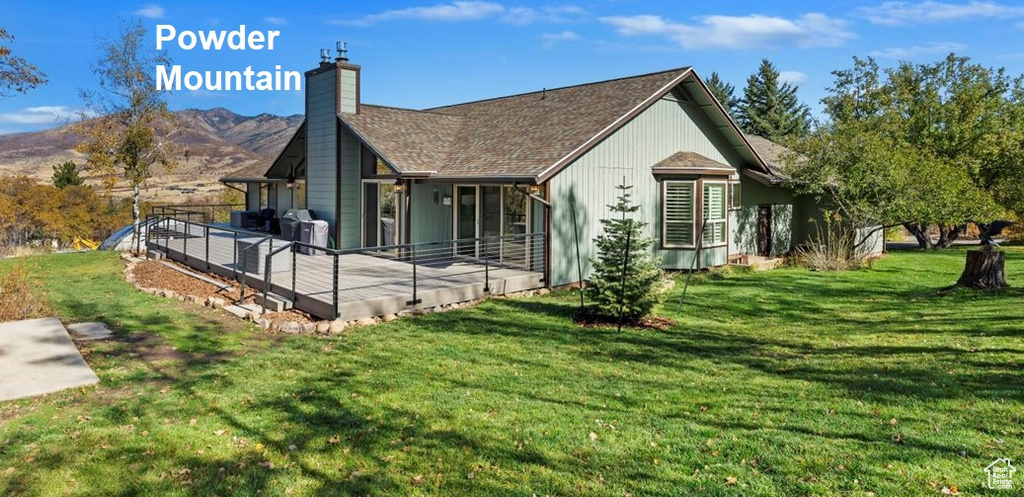 Back of house featuring a deck with mountain view, a yard, and a chimney