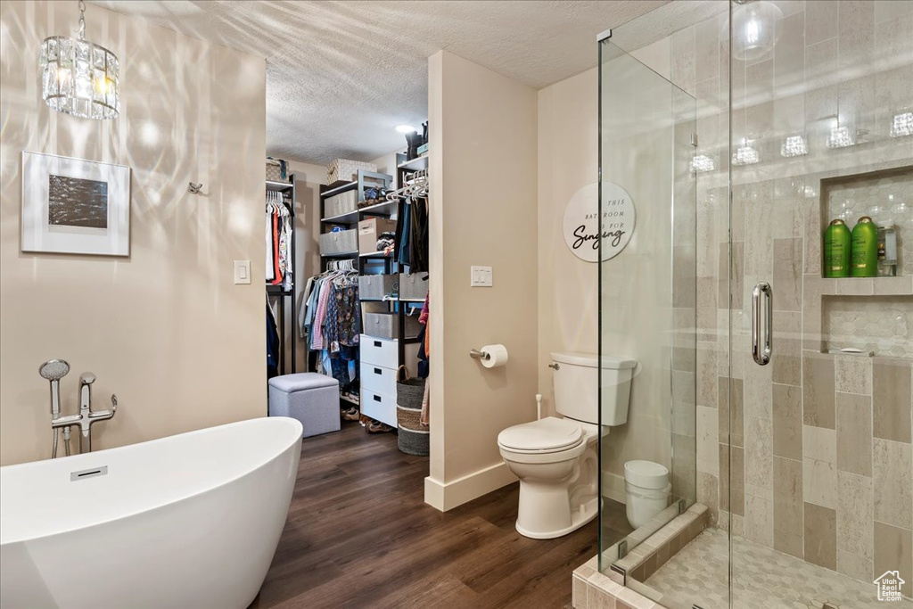 Full bathroom with a soaking tub, a stall shower, a walk in closet, wood finished floors, and a textured ceiling