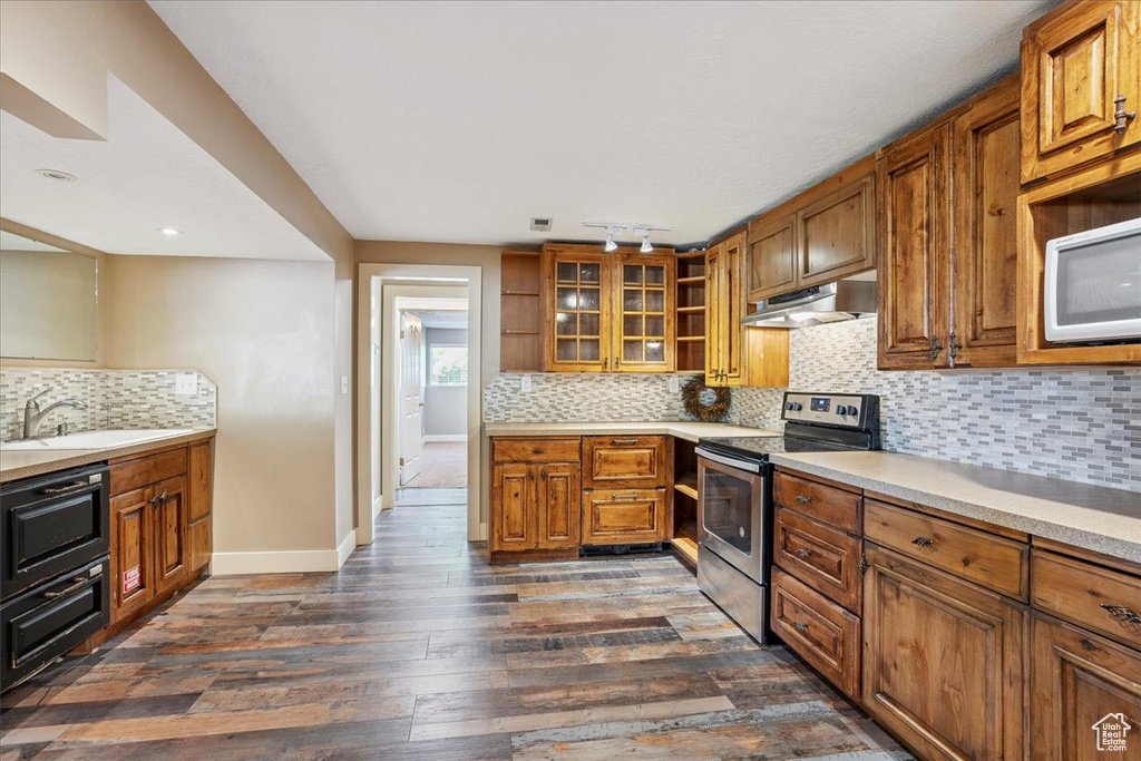 Kitchen featuring electric stove, white microwave, under cabinet range hood, and brown cabinets