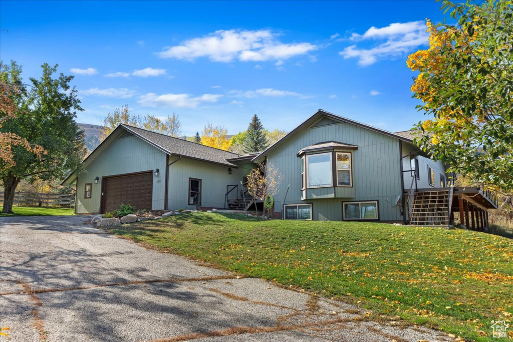 View of front facade with stairs, an attached garage, a front yard, and driveway