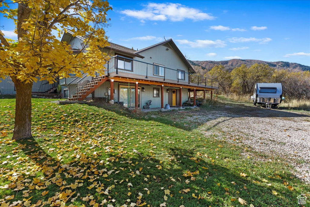 View of front of home with stairs, a deck with mountain view, a front yard, and gravel driveway