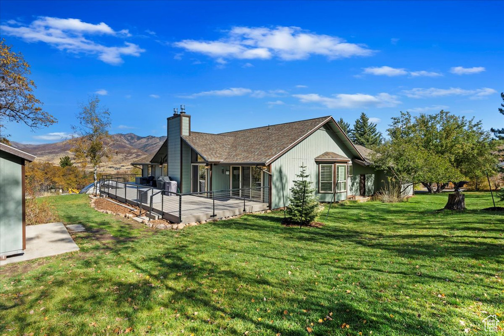 Back of house with a chimney, a lawn, and a deck with mountain view