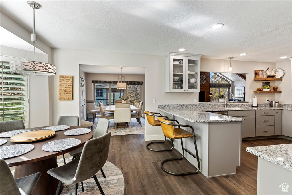Kitchen with a textured ceiling, glass insert cabinets, dark wood-style flooring, a peninsula, and pendant lighting